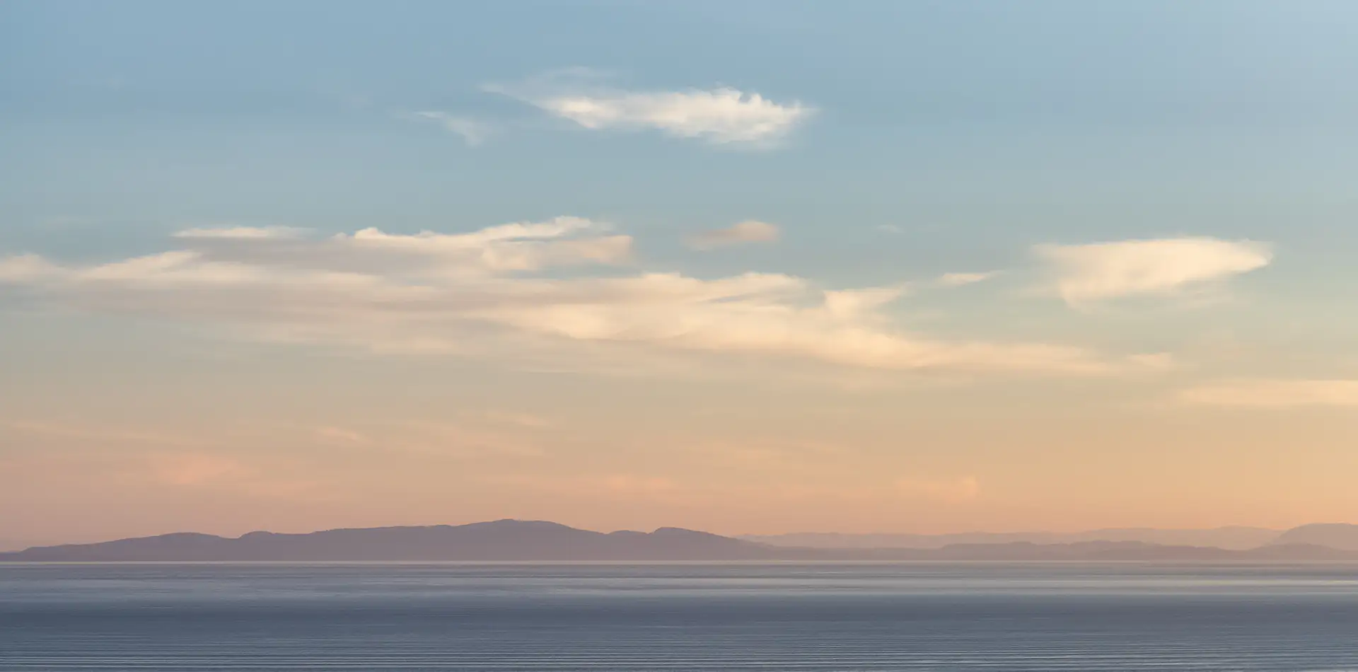 A calm horizon at sunrise or dusk—soft light over land or water