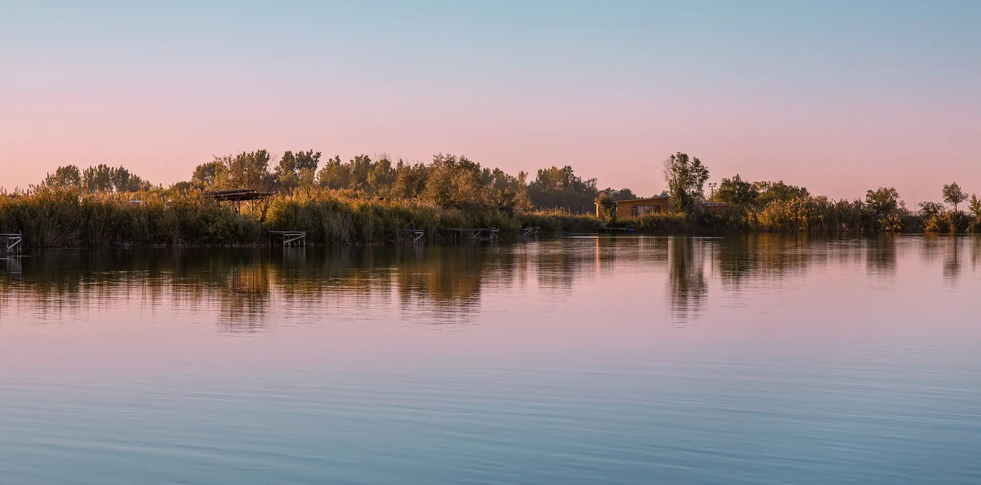 A wide panoramic view of a calm lake at dawn with soft sunlight reflecting on the water, symbolizing a new day of hope and peace.