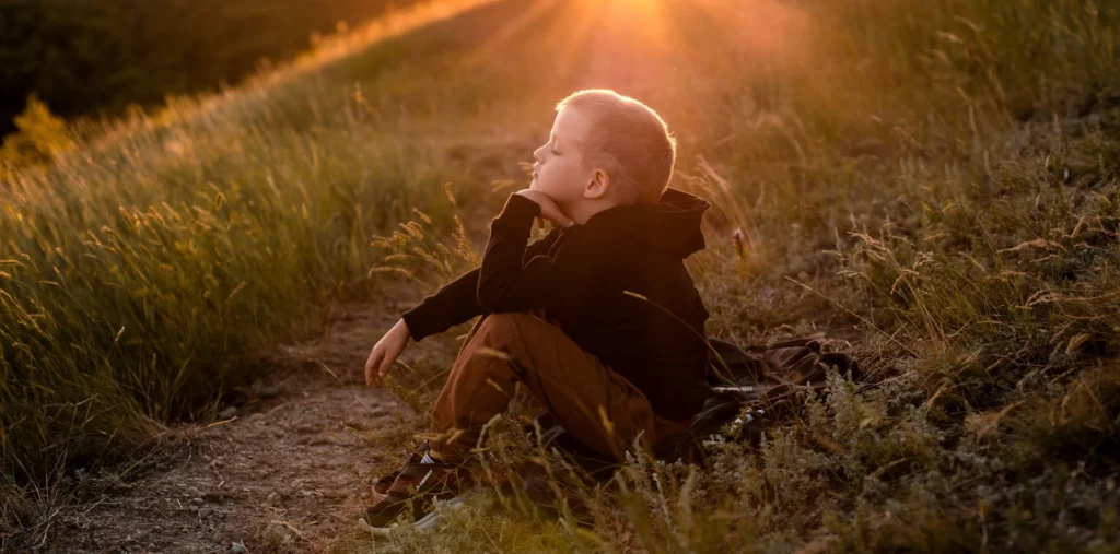 A child sitting alone in a sunlit field, symbolising the inner child and the journey toward emotional healing