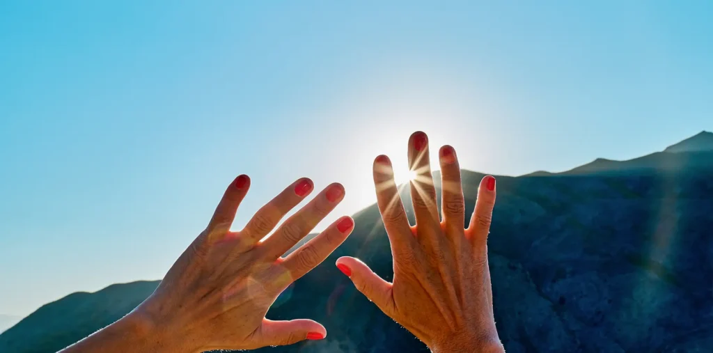 Hands reaching upward toward golden light rays symbolizing a prayer for creative energy and divine purpose