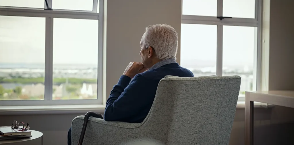 An elderly person sitting by a sunlit window in quiet, peaceful contemplation