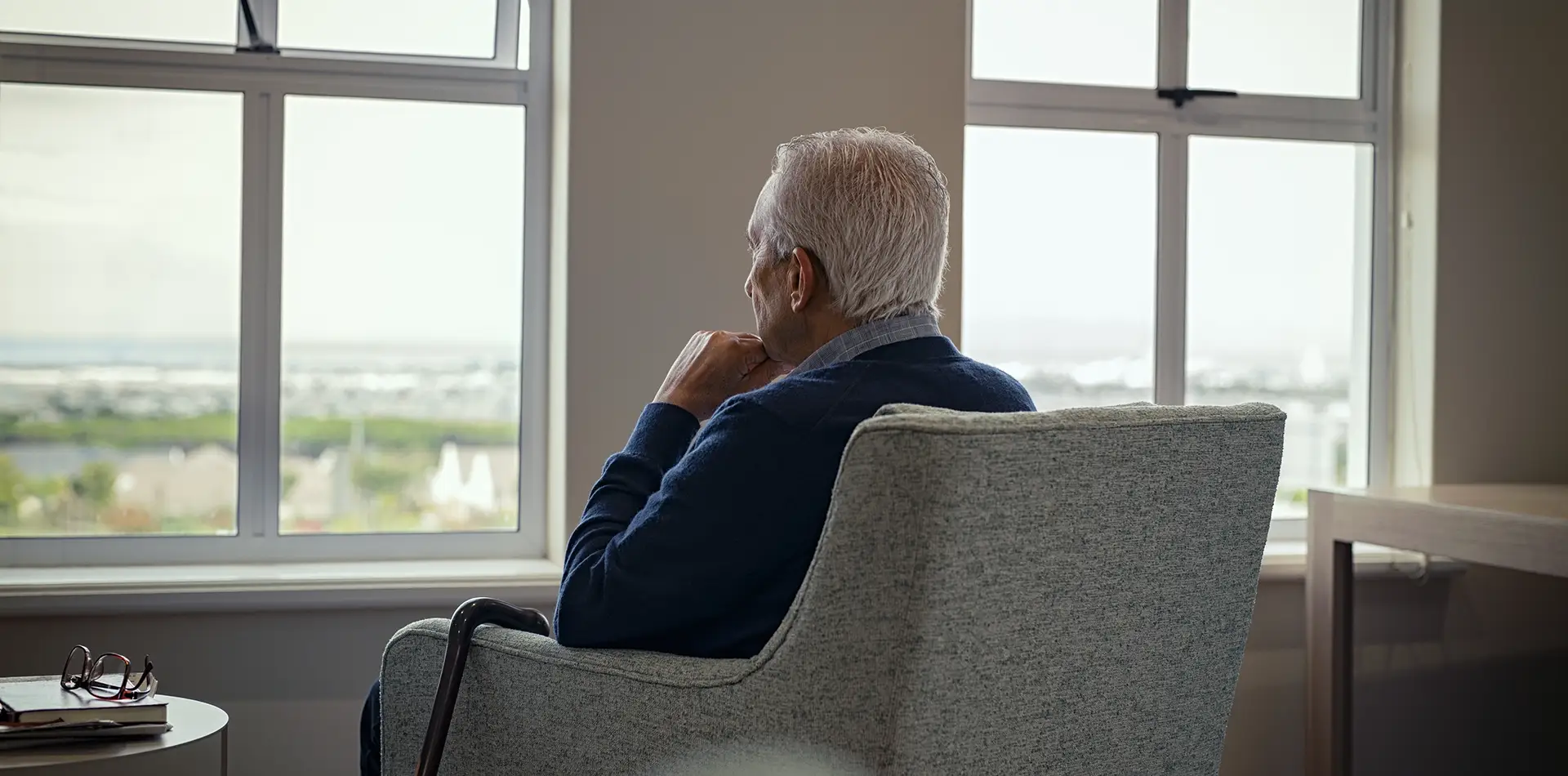An elderly person sitting by a sunlit window in quiet, peaceful contemplation