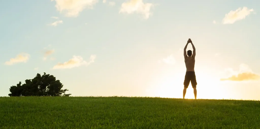 Person standing barefoot on green grass during a peaceful outdoor morning meditation at sunrise
