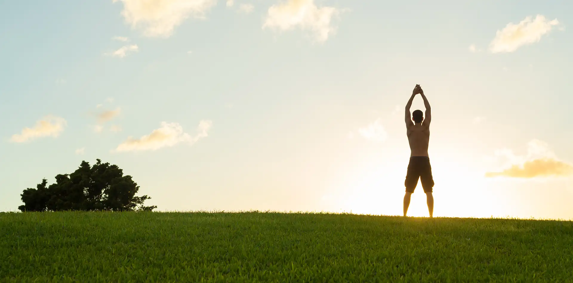 Person standing barefoot on green grass during a peaceful outdoor morning meditation at sunrise