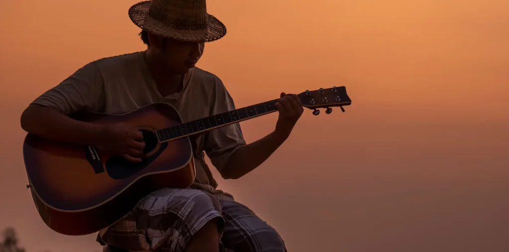 A man playing acoustic guitar outdoors in warm golden light, expressing passion and creative joy