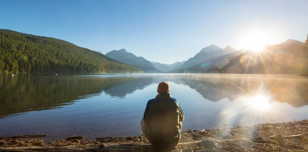 A peaceful person sitting beside a calm lake at sunrise