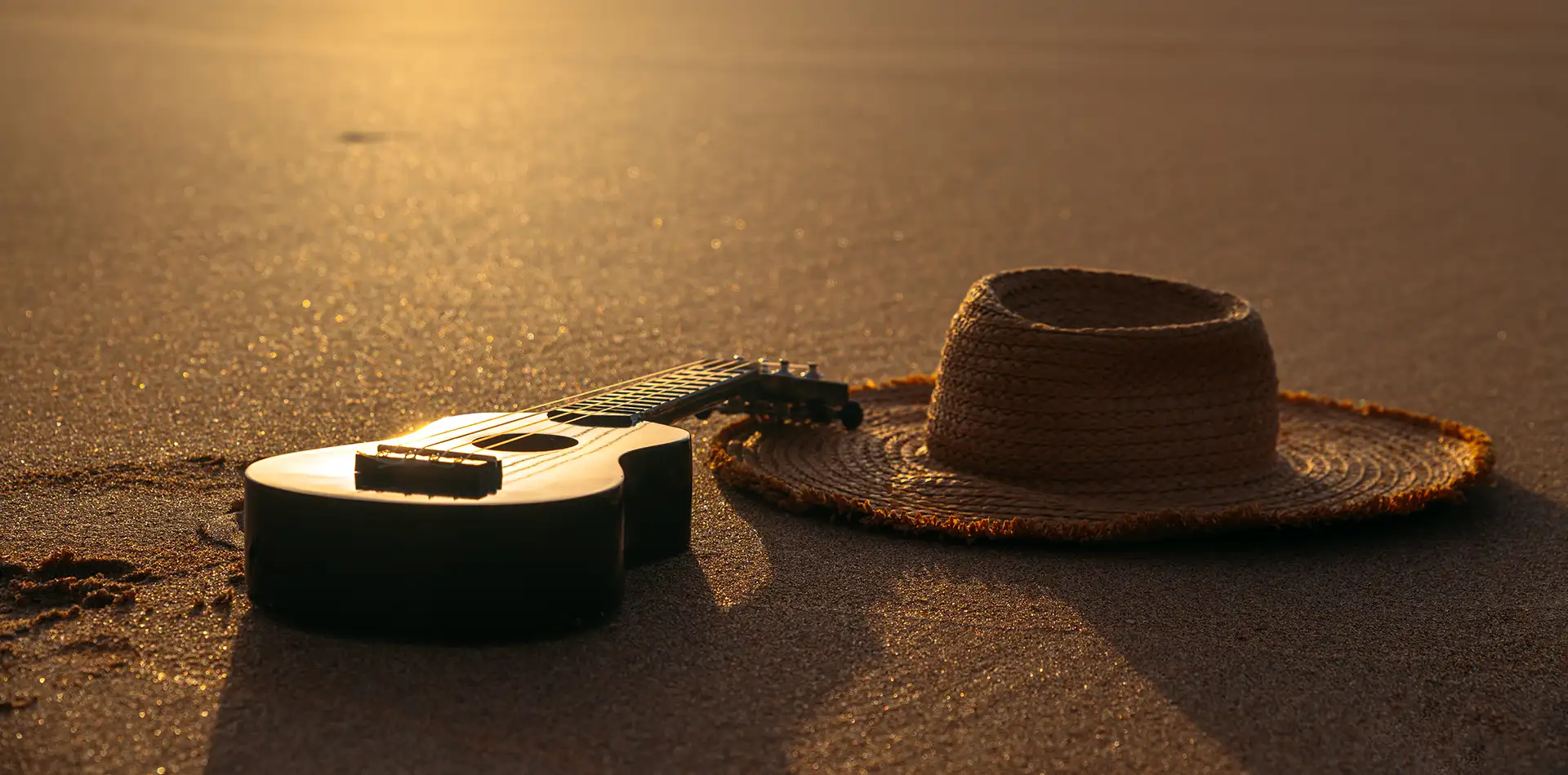 Acoustic guitar resting on the sand of a quiet tropical beach as the sun rises over the ocean