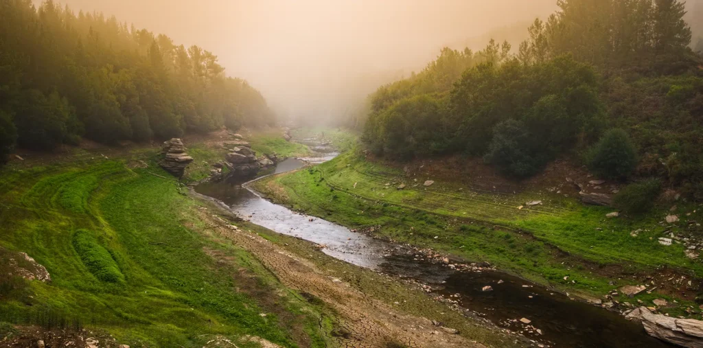 A gentle river winding through misty green mountains at sunrise, evoking natural flow and inner peace.