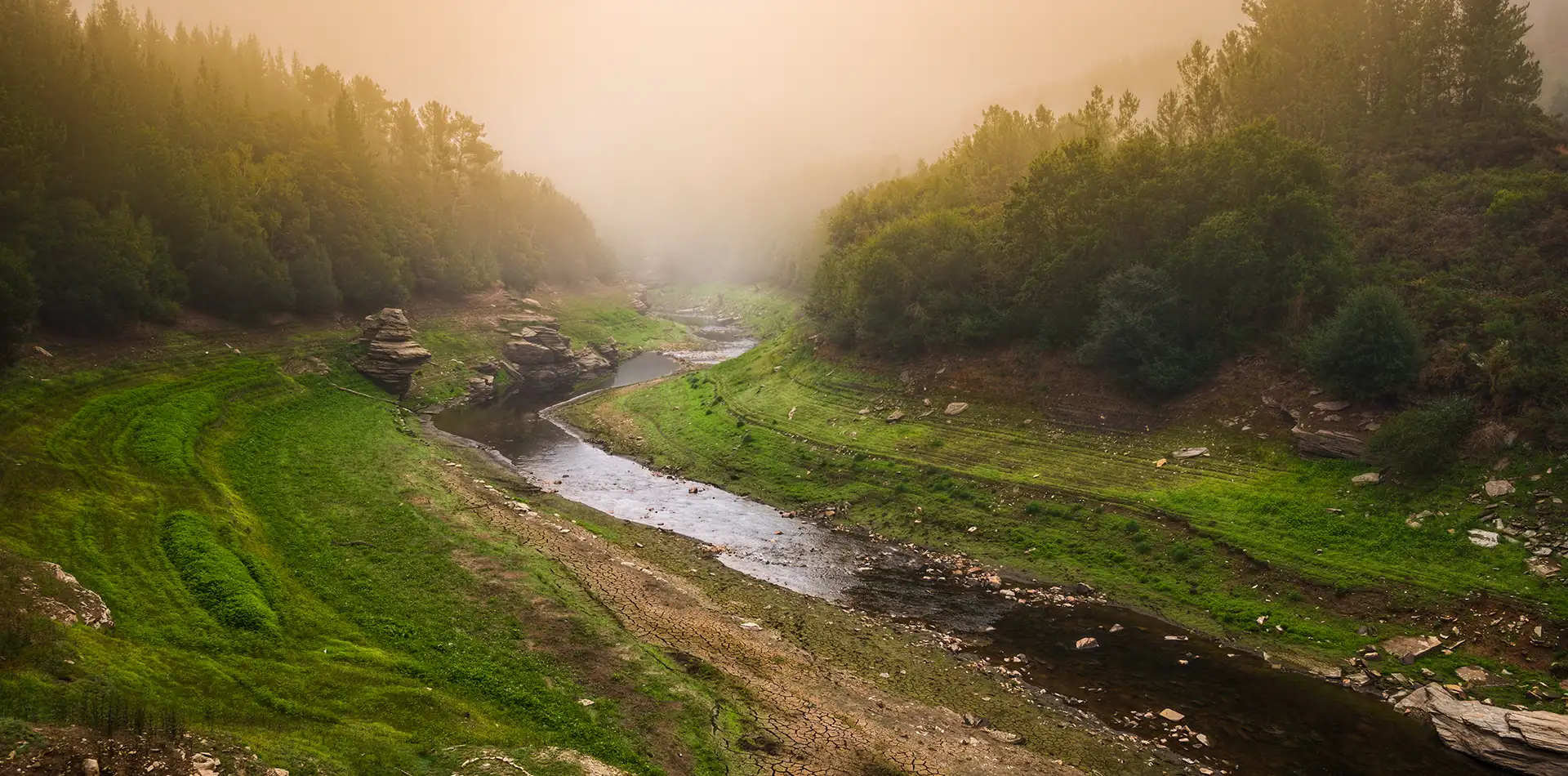 A gentle river winding through misty green mountains at sunrise, evoking natural flow and inner peace.