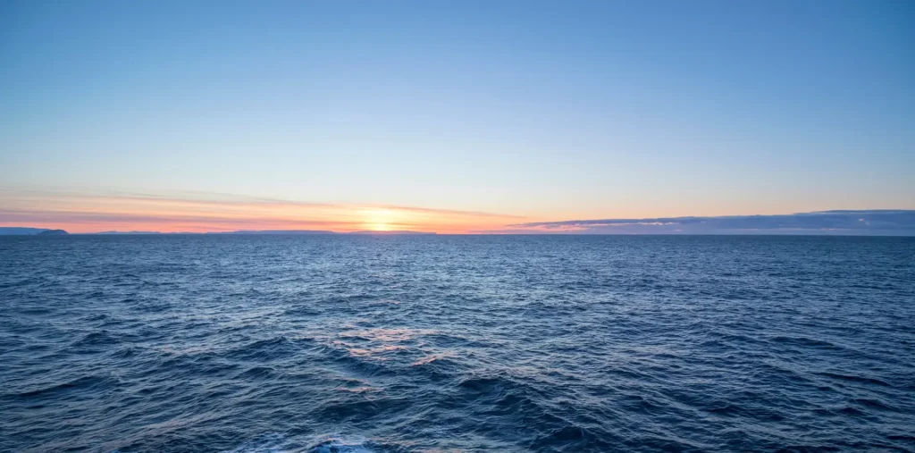 Soft golden light over calm ocean waves rolling toward a distant horizon at dawn