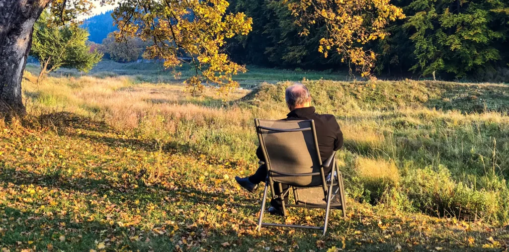 An older man sitting peacefully outdoors in nature, reflecting on the meaning of life