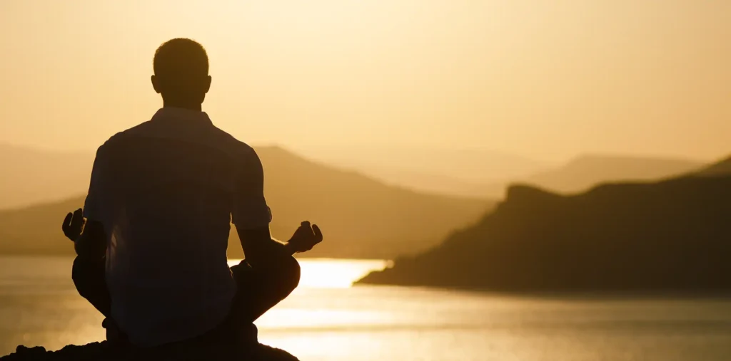 Person meditating beside a calm lake at sunrise, sensing the flow of energy and inner balance in nature