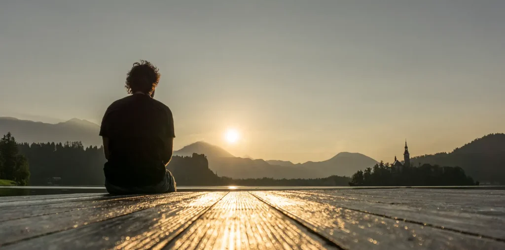 Older person sitting quietly in nature at sunrise, reflecting on spirituality and getting older with a sense of calm.