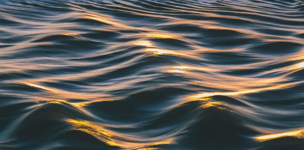 Glowing sound waves rippling across calm water at sunrise, reflecting the frequencies of love and peace