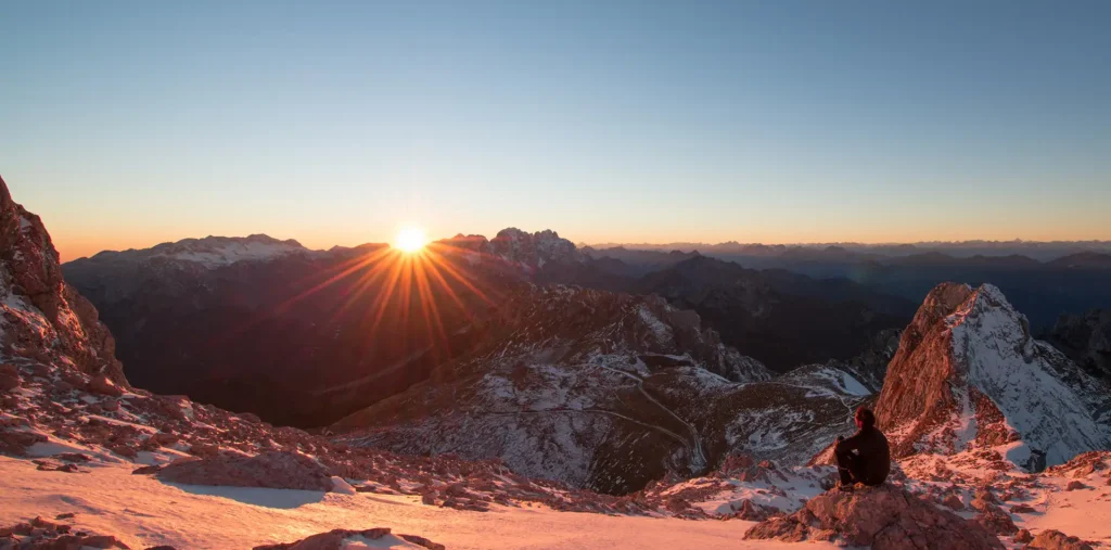 Person meditating at sunrise on a snow-capped mountain peak bathed in soft golden light