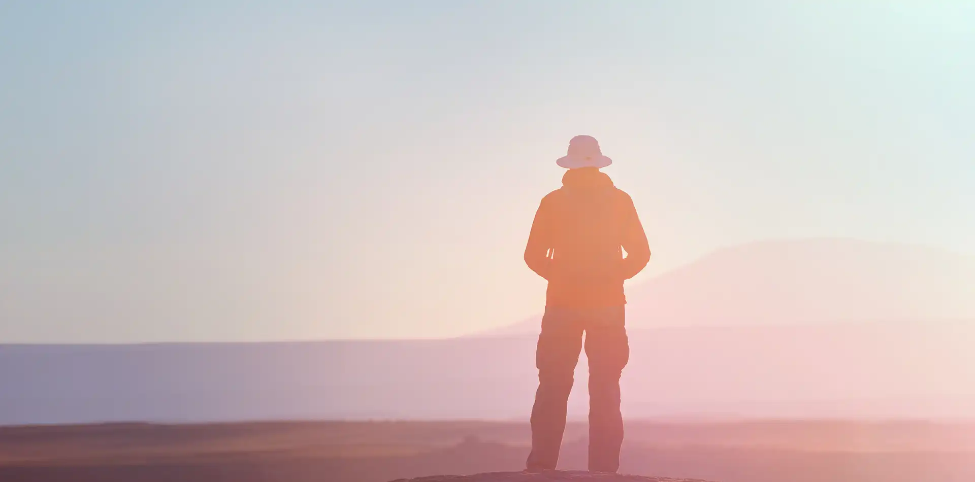 A person standing on a hilltop facing a glowing sunrise, symbolizing the search for meaning and inner consciousness