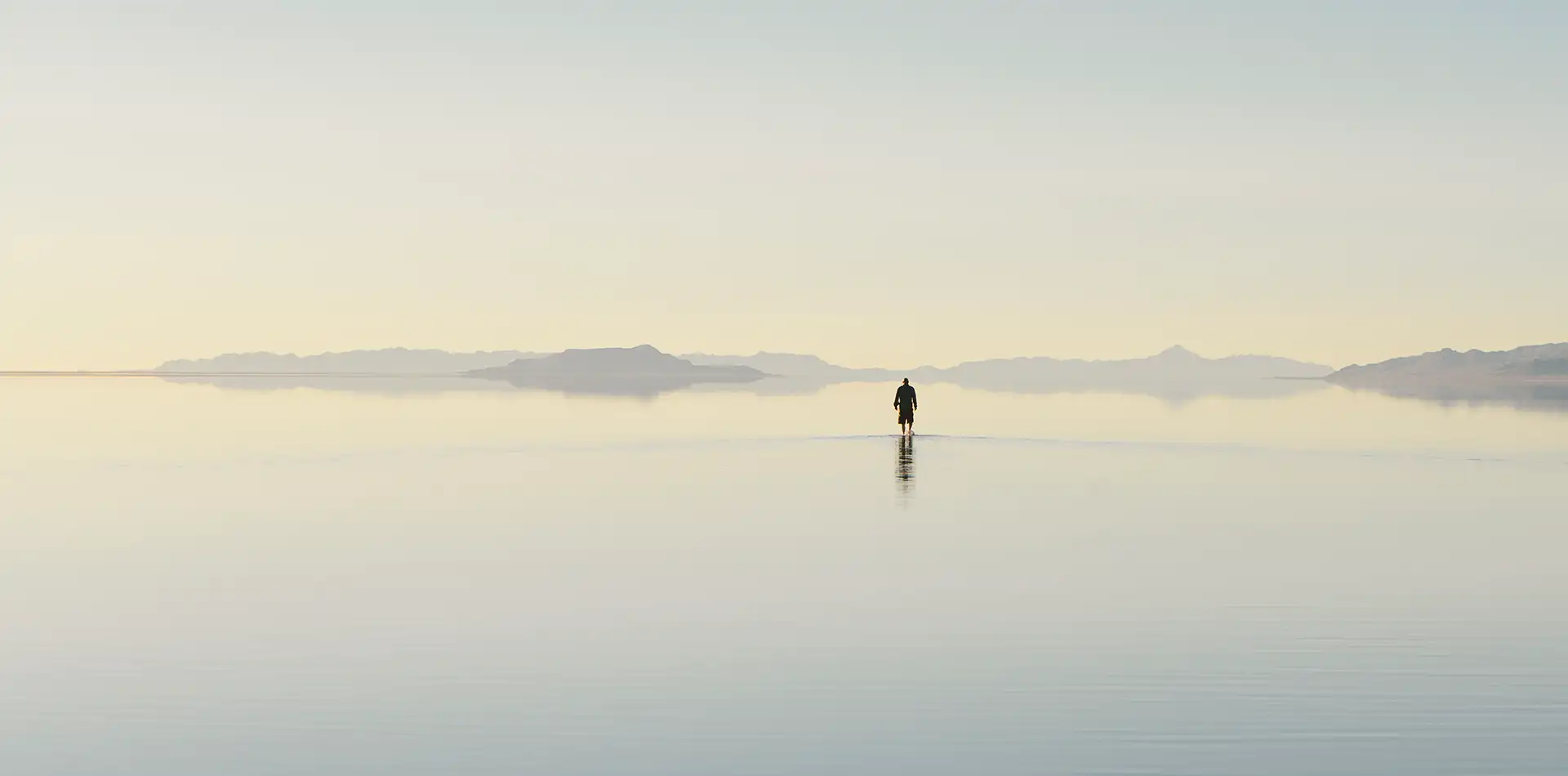 A person standing quietly at sunrise beside a calm shoreline, representing the foundation of love and peace at the beginning of an inner journey.