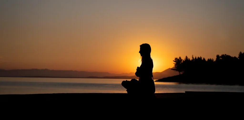 Silhouette of a person kneeling with clasped hands in warm golden light at sunrise