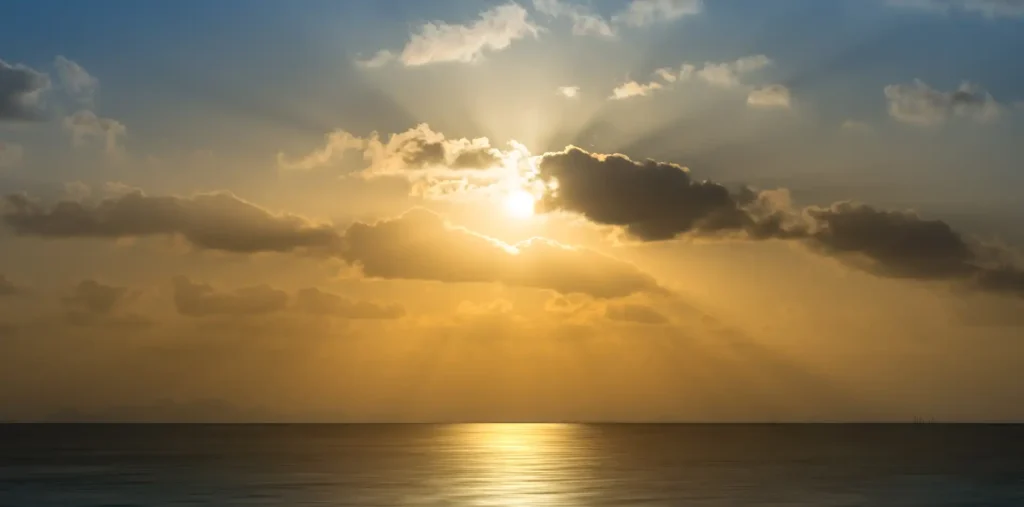 Golden sunrise light breaking through clouds over a calm, peaceful ocean