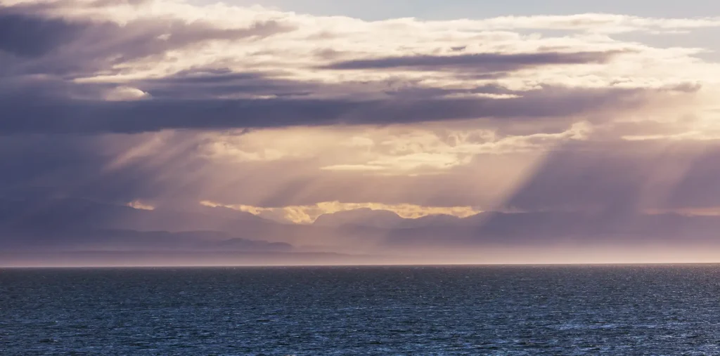Soft golden light rays breaking through clouds over a calm horizon