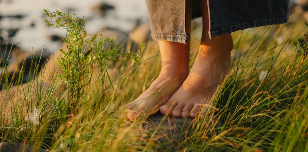 Person standing barefoot on grass at sunrise practicing grounding and inner reflection