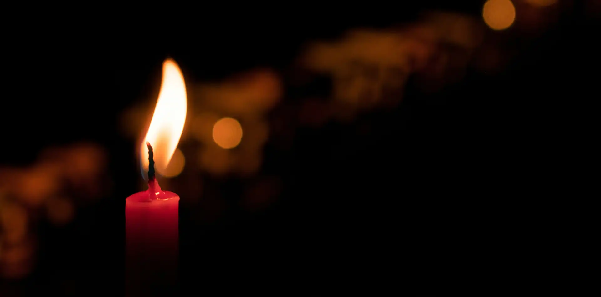 A single candle flame casting warm golden light against a dark background
