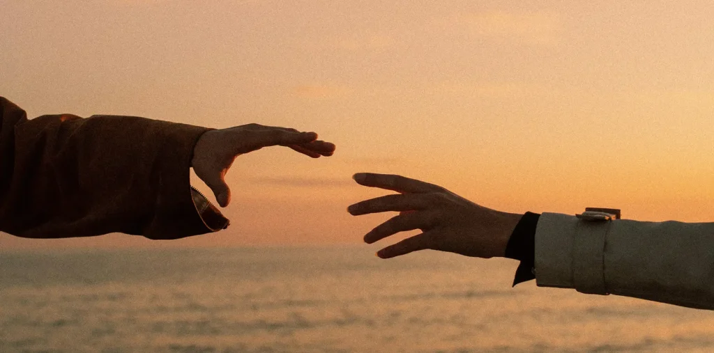 Two hands reaching toward one another in warm sunset light representing connection and forgiveness