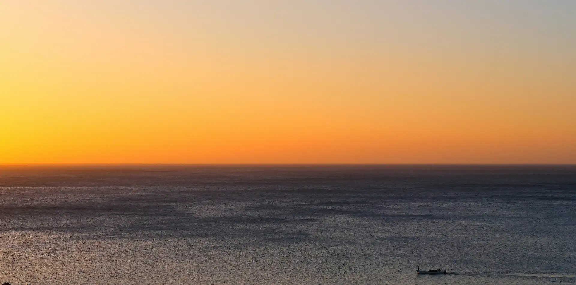 Soft golden sunrise light spreading across a calm ocean horizon at daybreak