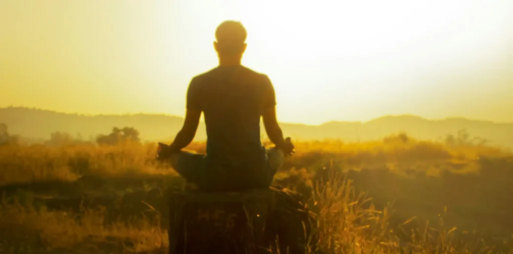 Silhouette of a person facing a golden sunrise on a peaceful hilltop