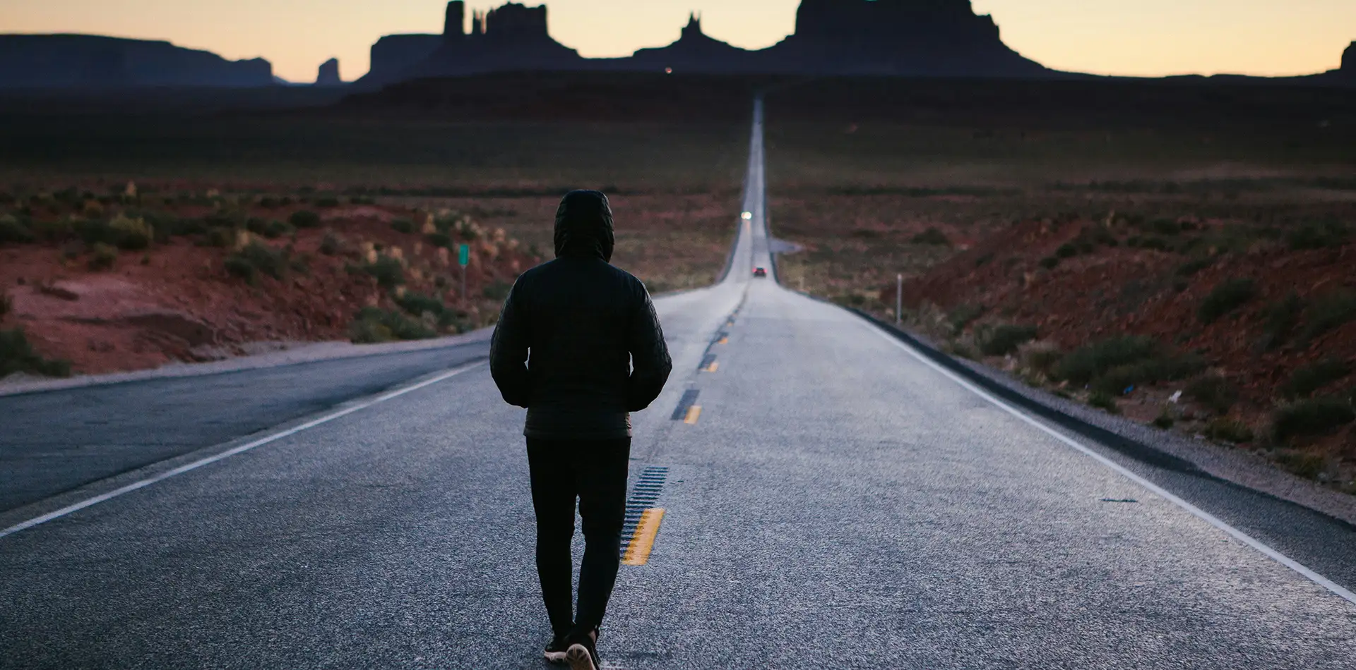 A lone figure walking a quiet open road toward soft dawn light, representing perseverance and hope