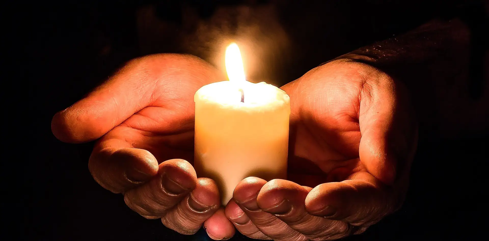 Cupped hands holding a glowing candle with soft radiating light energy