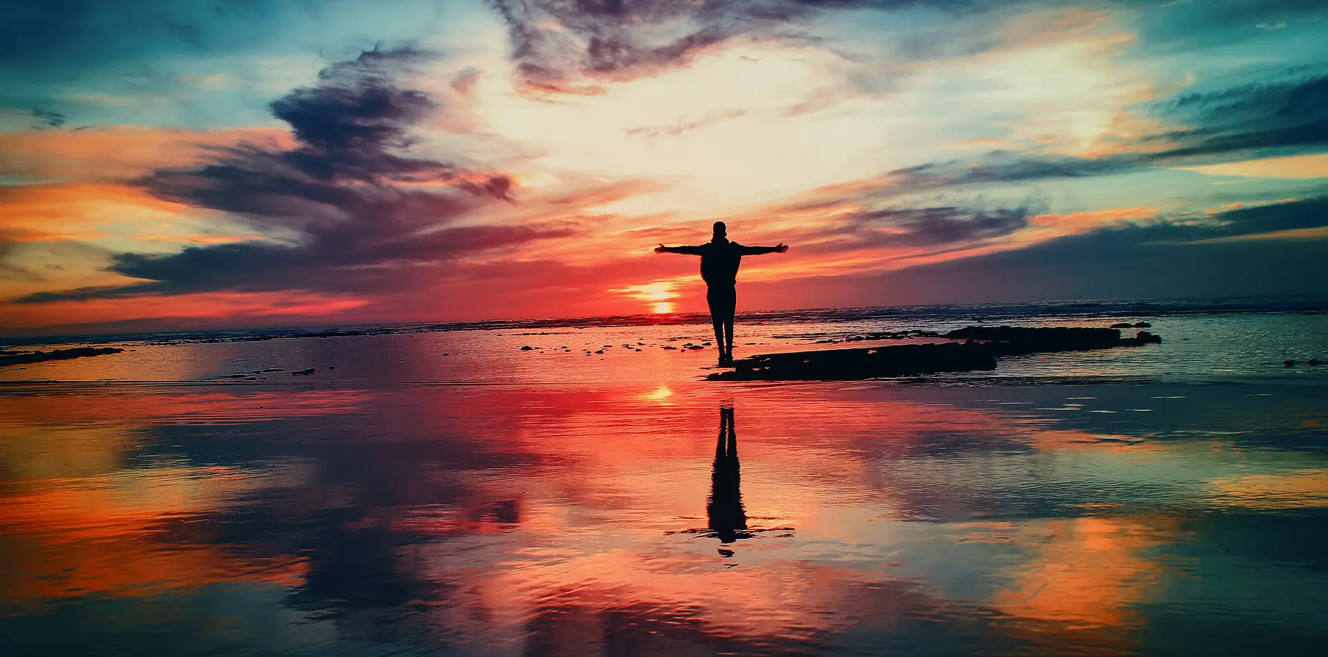 A lone figure at the shoreline as sea and sky blend together in soft golden morning light