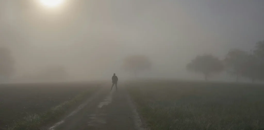 Silhouette of a person walking a misty path toward a glowing light at sunrise