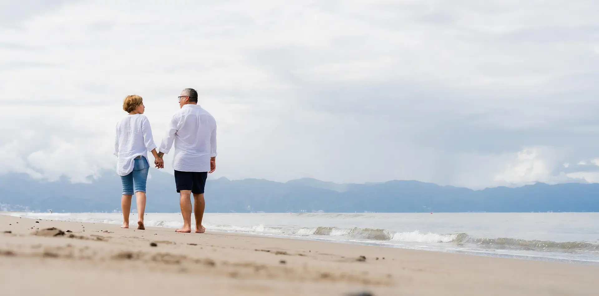 Older couple holding hands walking a quiet path at sunset in soft golden light