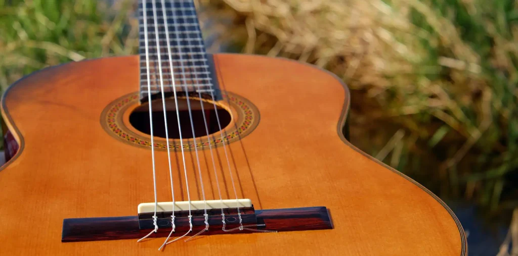 Acoustic guitar resting outdoors in soft golden morning light with a blurred green background