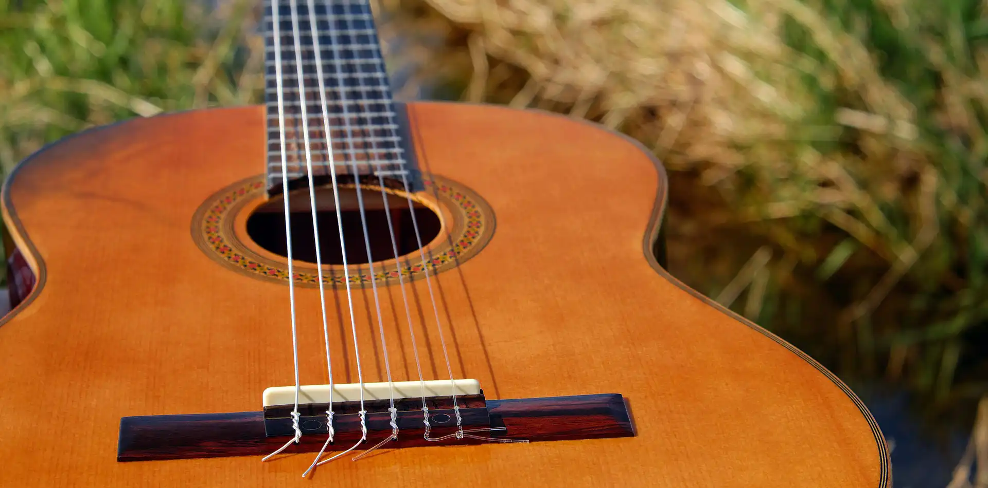 Acoustic guitar resting outdoors in soft golden morning light with a blurred green background