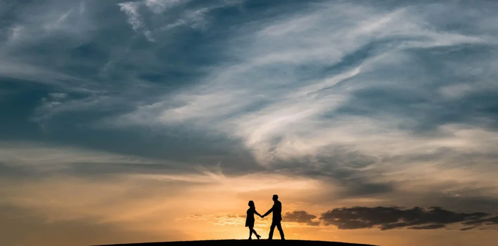 Elderly couple holding hands while watching a golden sunrise over soft clouds